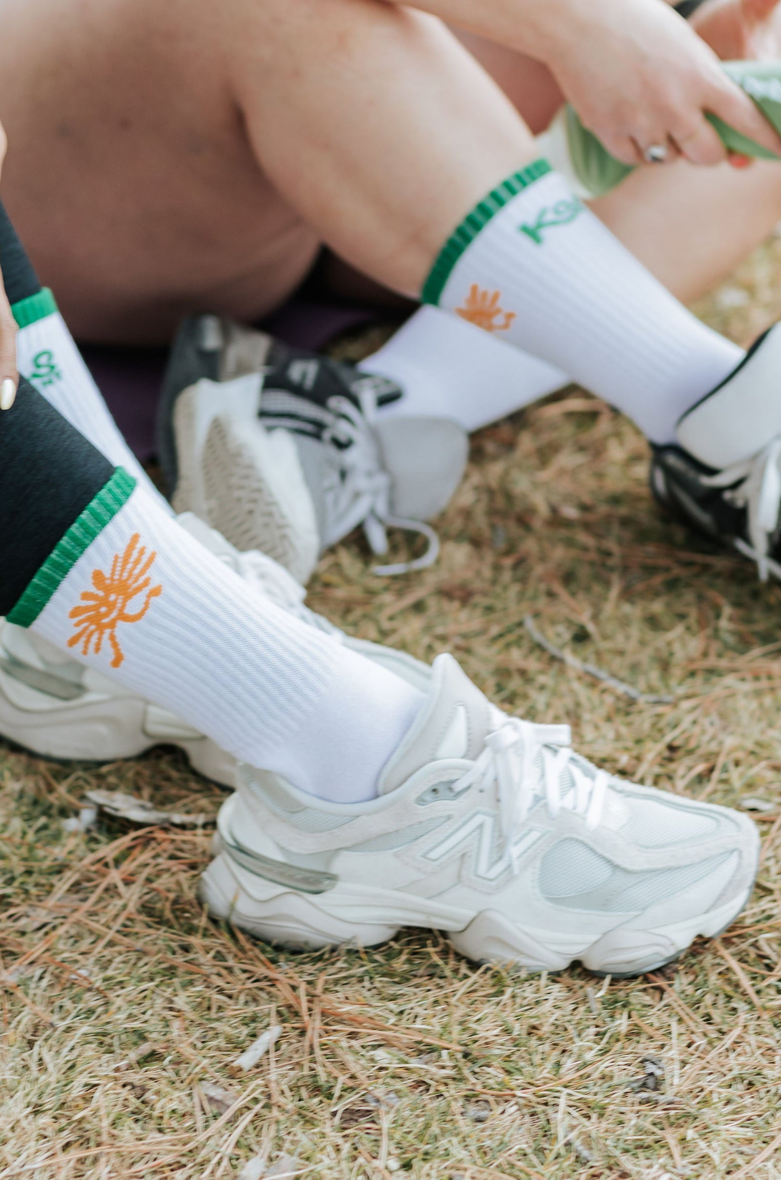 Two people sitting on the ground wearing socks with a logo.