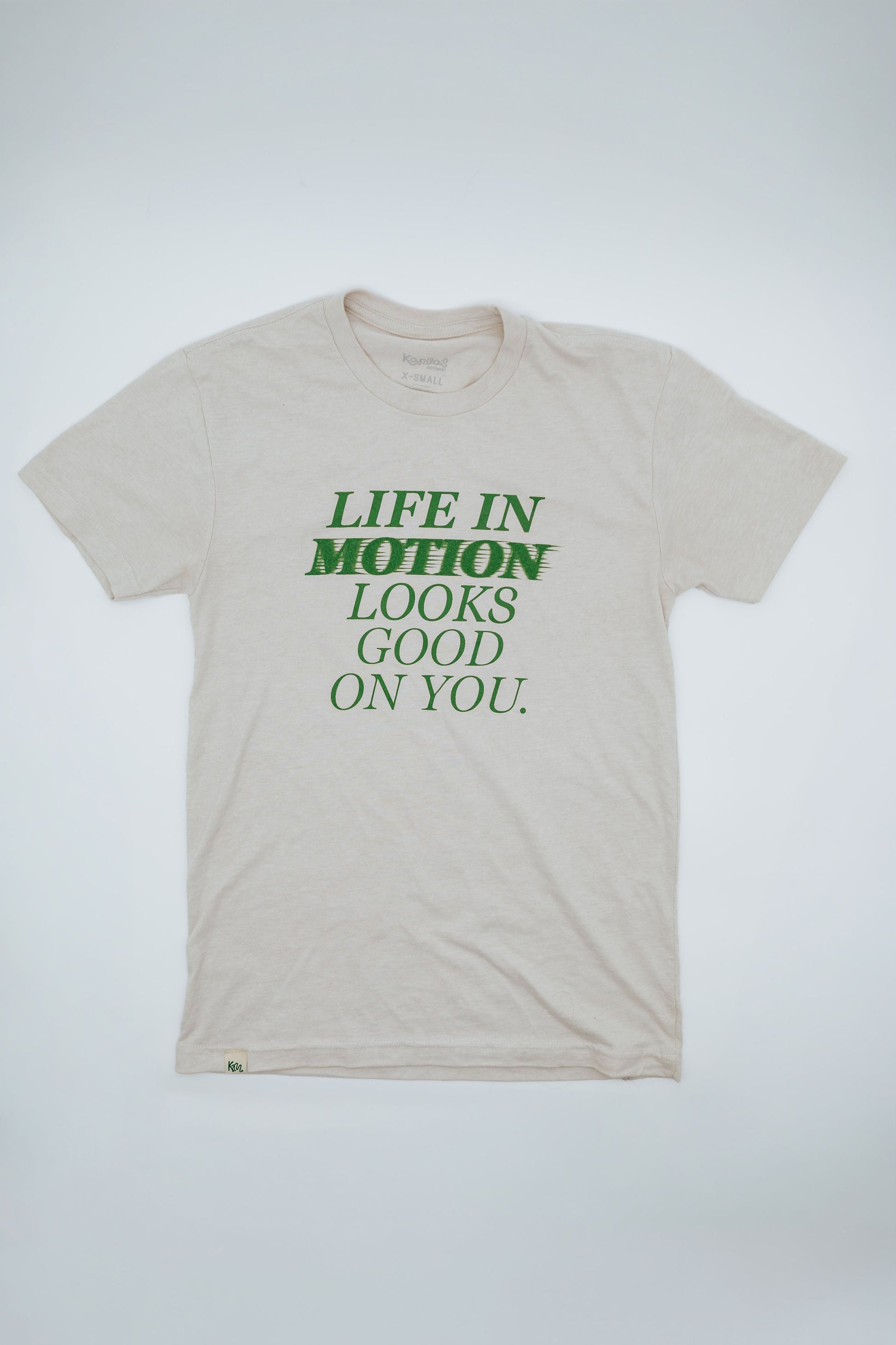 Beige short sleeve t-shirt with green text "Life in motion looks good on you" on a white background