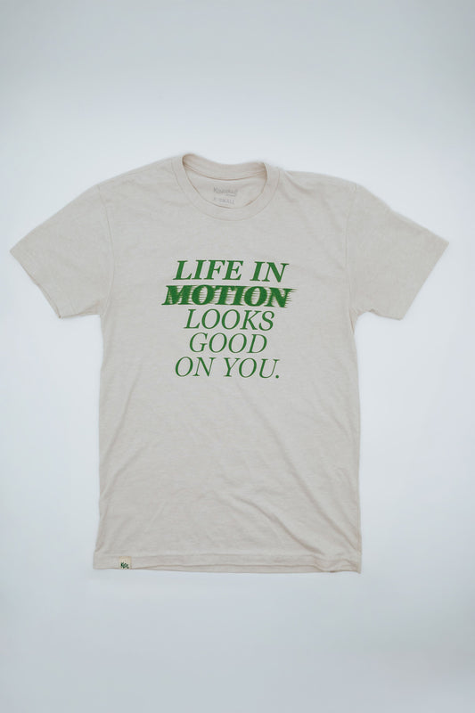 Beige short sleeve t-shirt with green text "Life in motion looks good on you" on a white background