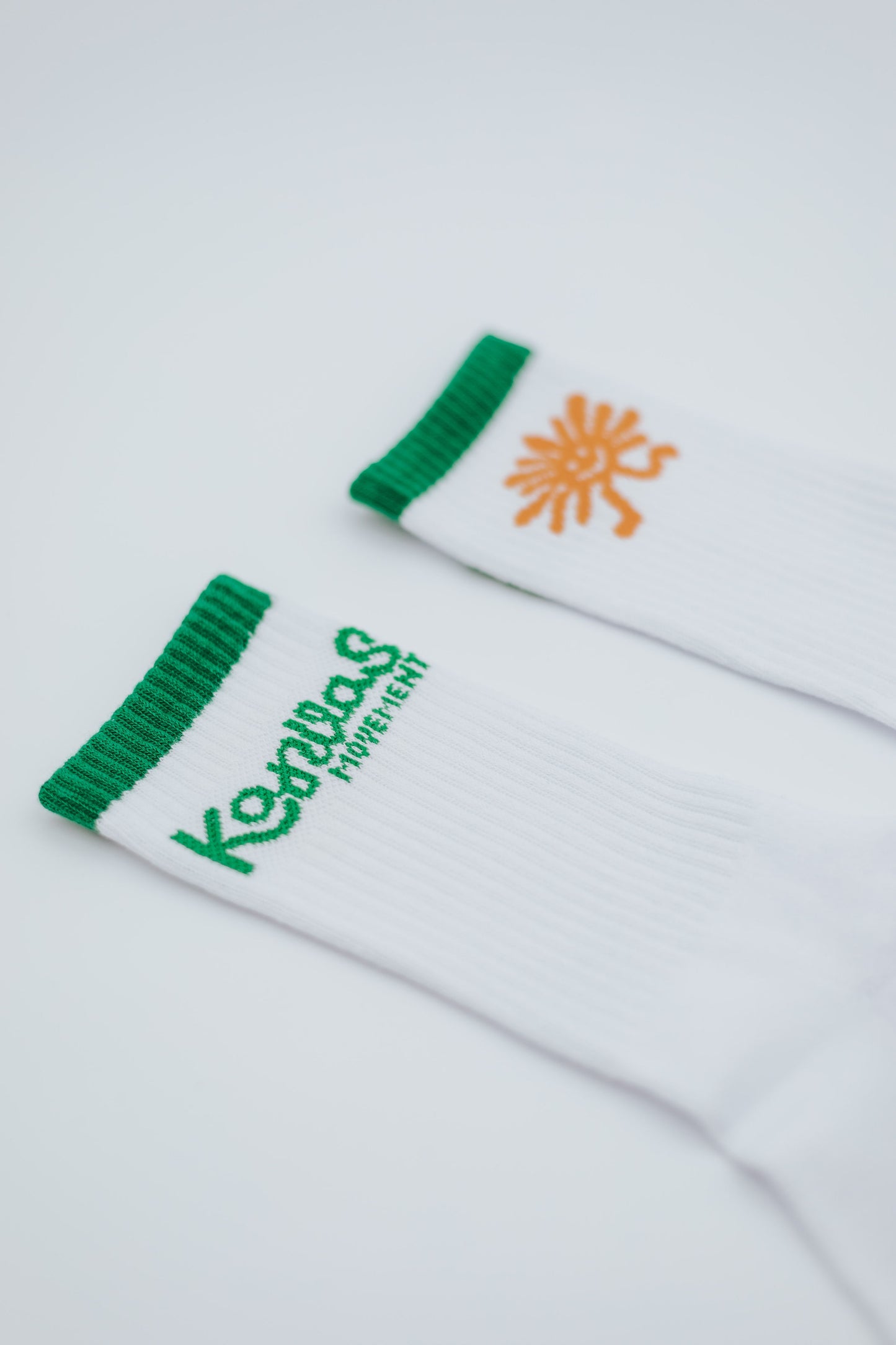 White socks with green ribbing and orange logo on a light gray background