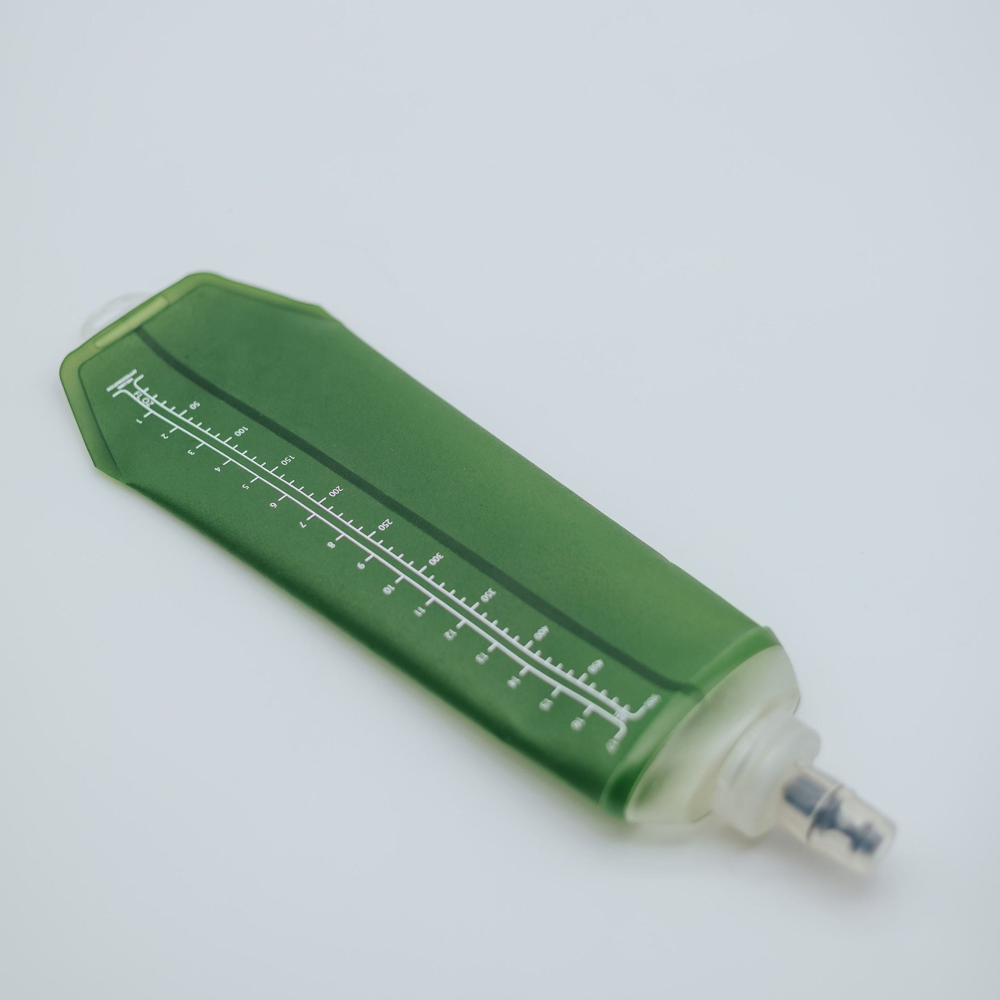 A green soft flask with white printed measurement markings and a clear cap, photographed on a plain light background.