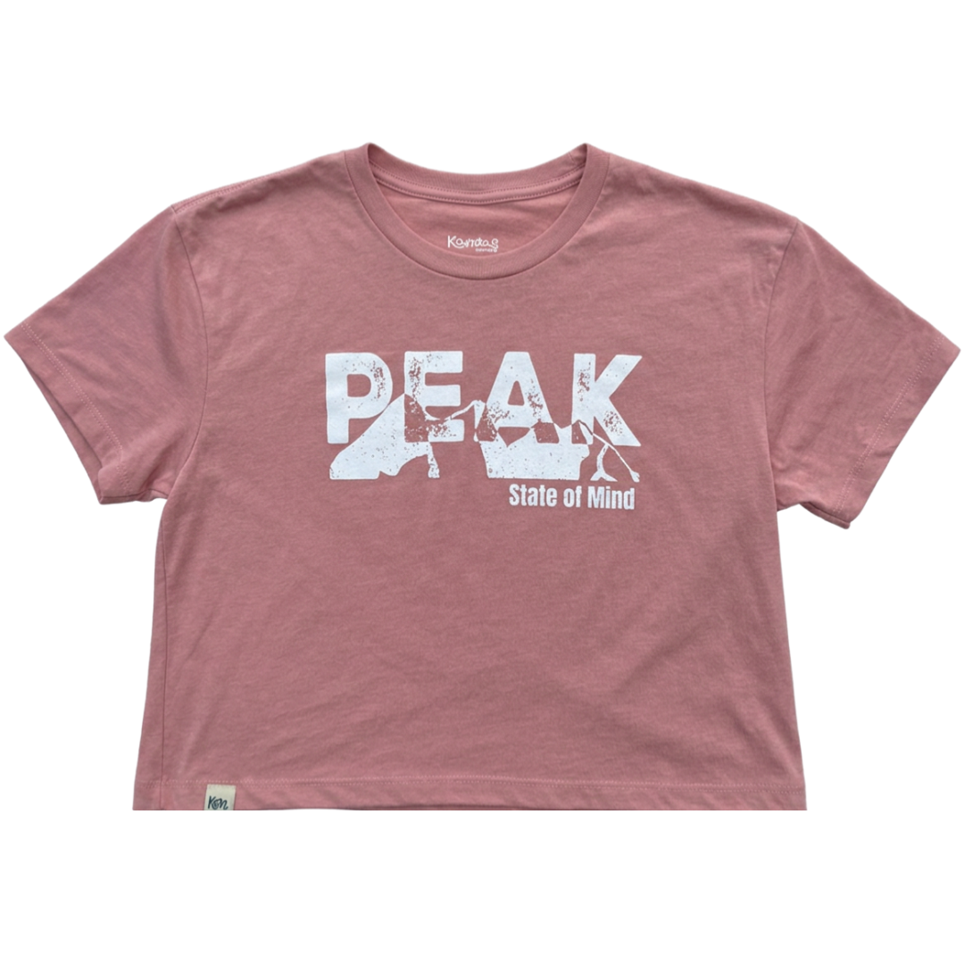 A dusty rose short-sleeve crop top t-shirt featuring a white graphic print of the word 'PEAK' with a mountain silhouette and the text 'State of Mind' underneath, displayed flat against a white background.