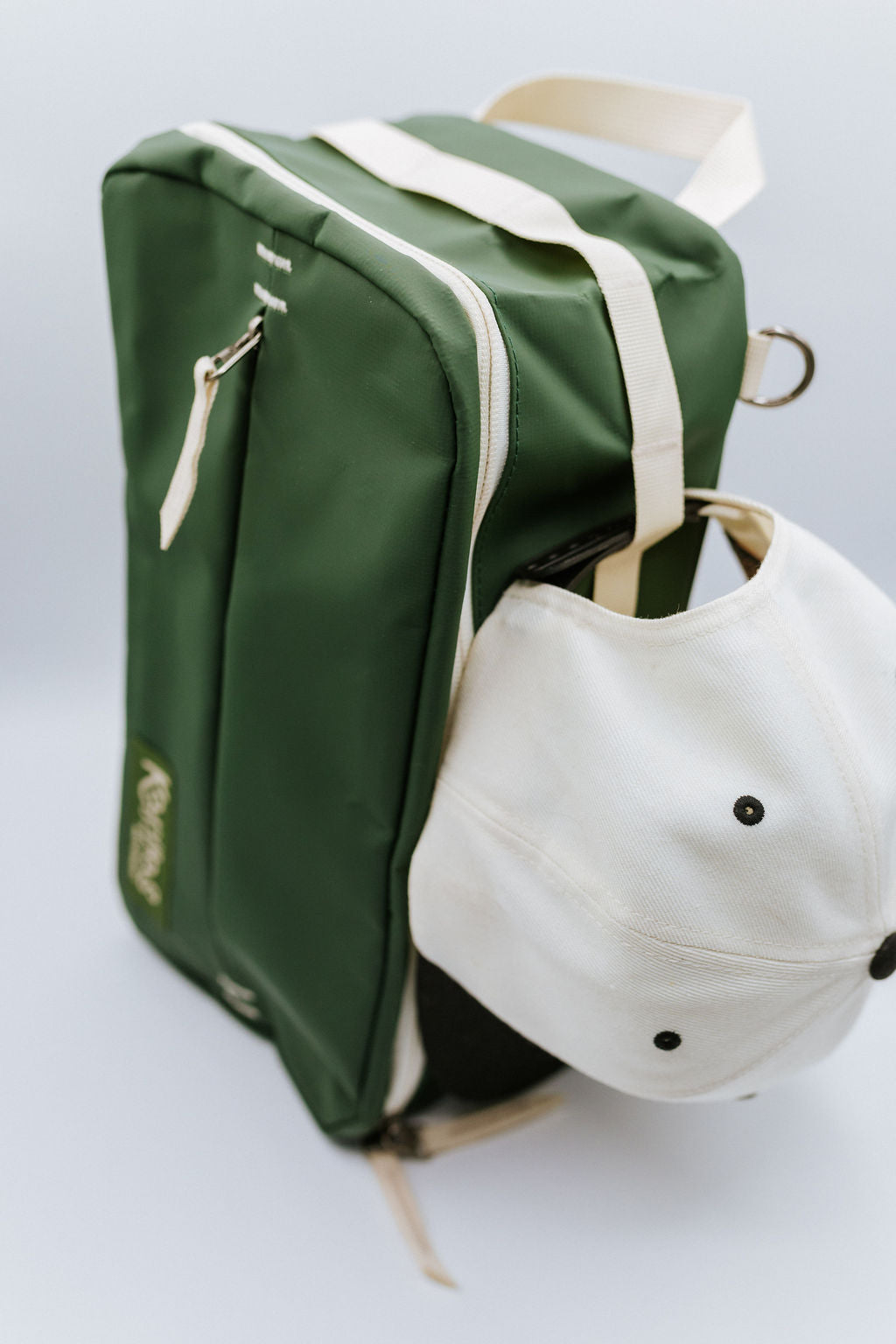 Green bag with a white hat attached to the bag on a light gray background