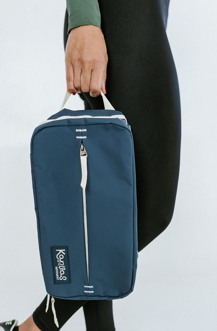 Person holding a blue shoe bag with a visible brand logo 'Kanvas Movement' on a white background